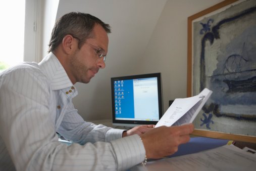 Man sitting at desk holding documents, side view
